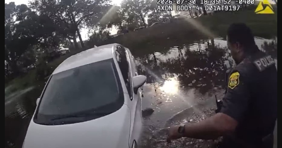 Clearwater Police Department body-camera frame showing an officer beside a partially submerged white car during a pond rescue on July 30, 2026.