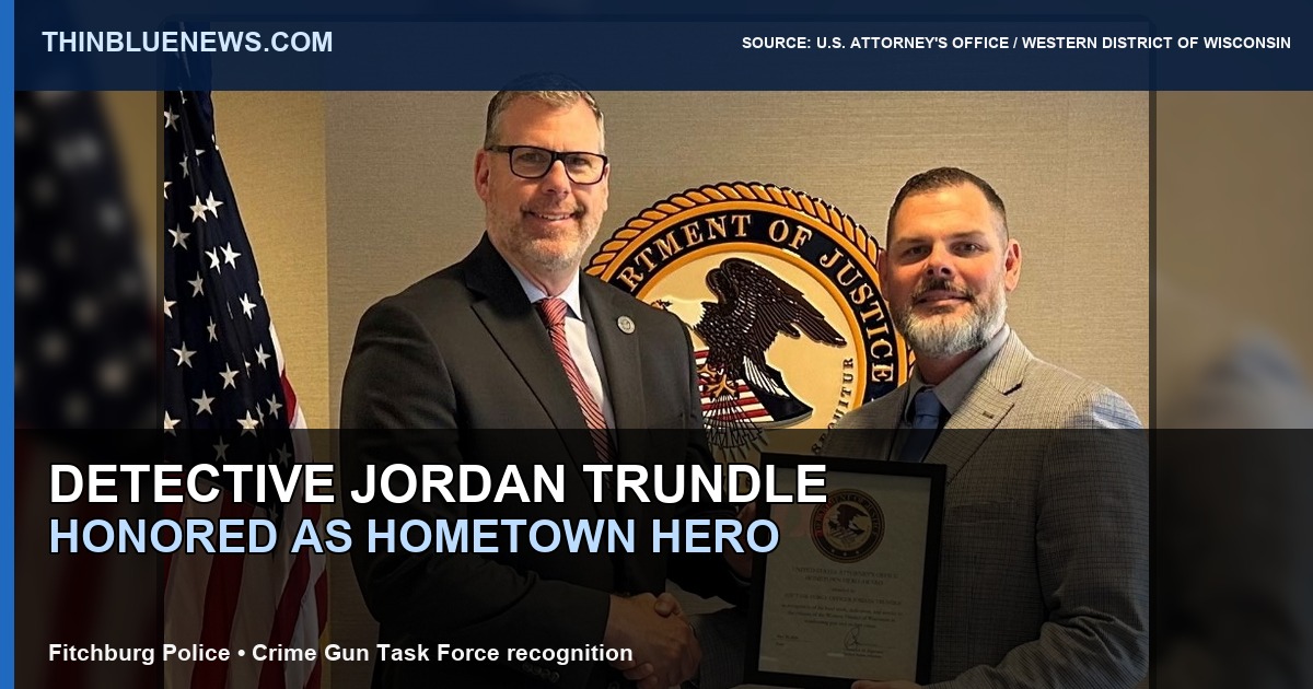 Official U.S. Attorney’s Office photo showing Fitchburg Detective Jordan Trundle receiving a Hometown Hero Award from U.S. Attorney Chadwick Elgersma; ThinBlueNews added headline and source labeling.