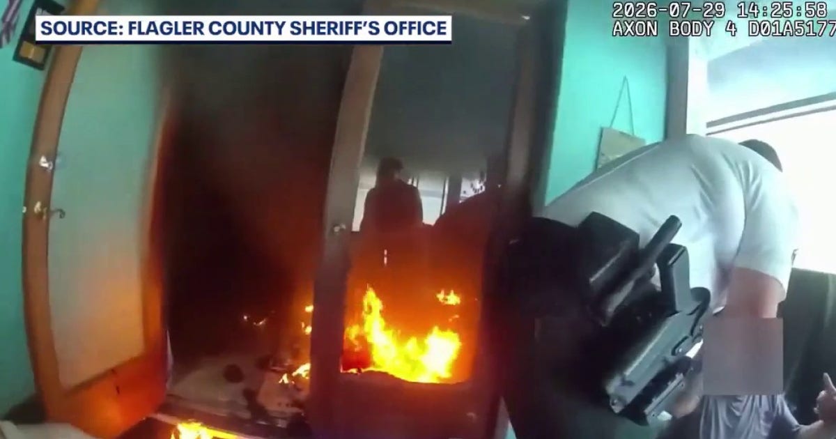 Flagler County Sheriff's Office body-camera frame showing deputies moving a homeowner away from flames inside a Palm Coast house on July 29, 2026.