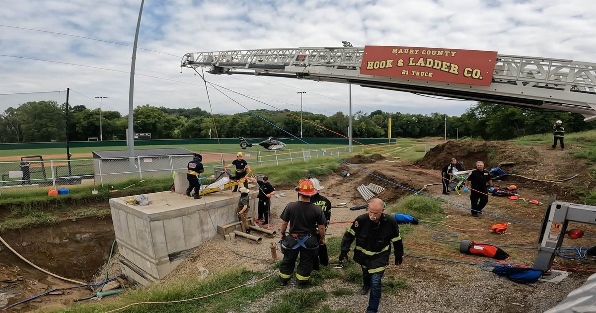 Maury County Fire Department firefighters using a hook-and-ladder truck, ropes and a rescue basket during a confined-space rescue at Santa Fe Unit School in Tennessee