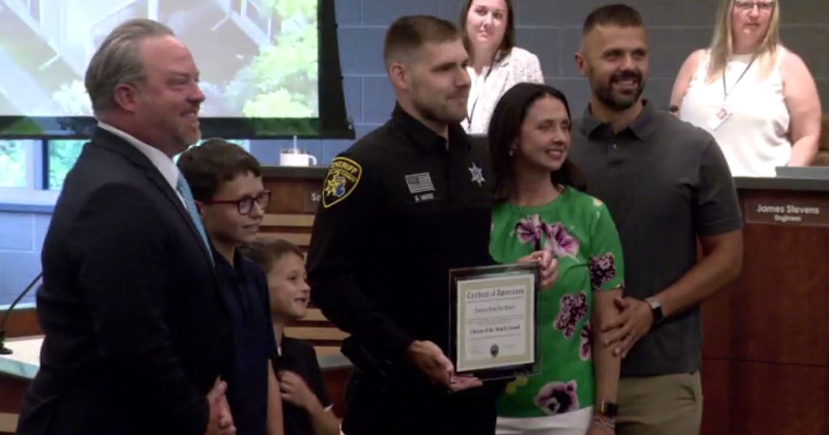 Oakland County Sheriff's Deputy Brandon Musse holding a framed recognition beside the rescued boys and their family during a public ceremony.