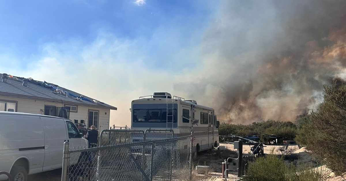 Smoke from the Thorn Fire rises behind a Boulevard, California, home as a van and recreational vehicle sit inside the property fence.