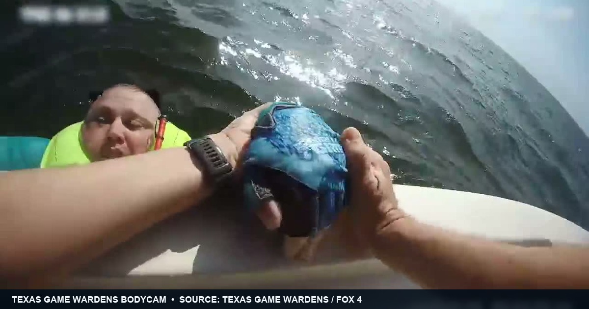 Texas Game Wardens body-camera frame showing rescuers gripping the hands of life-jacketed fisherman Steven Otto beside their boat on Lake Tawakoni.