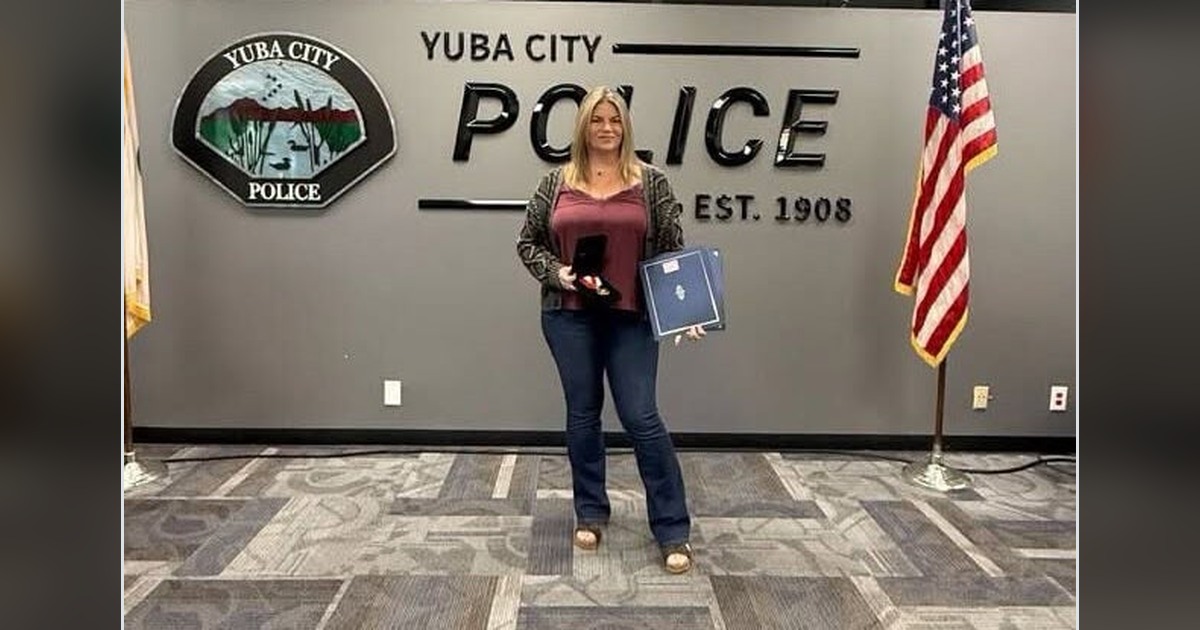 Yuba City Police Dispatcher Amelia Boom holding a lifesaving medal and certificate in front of the department sign
