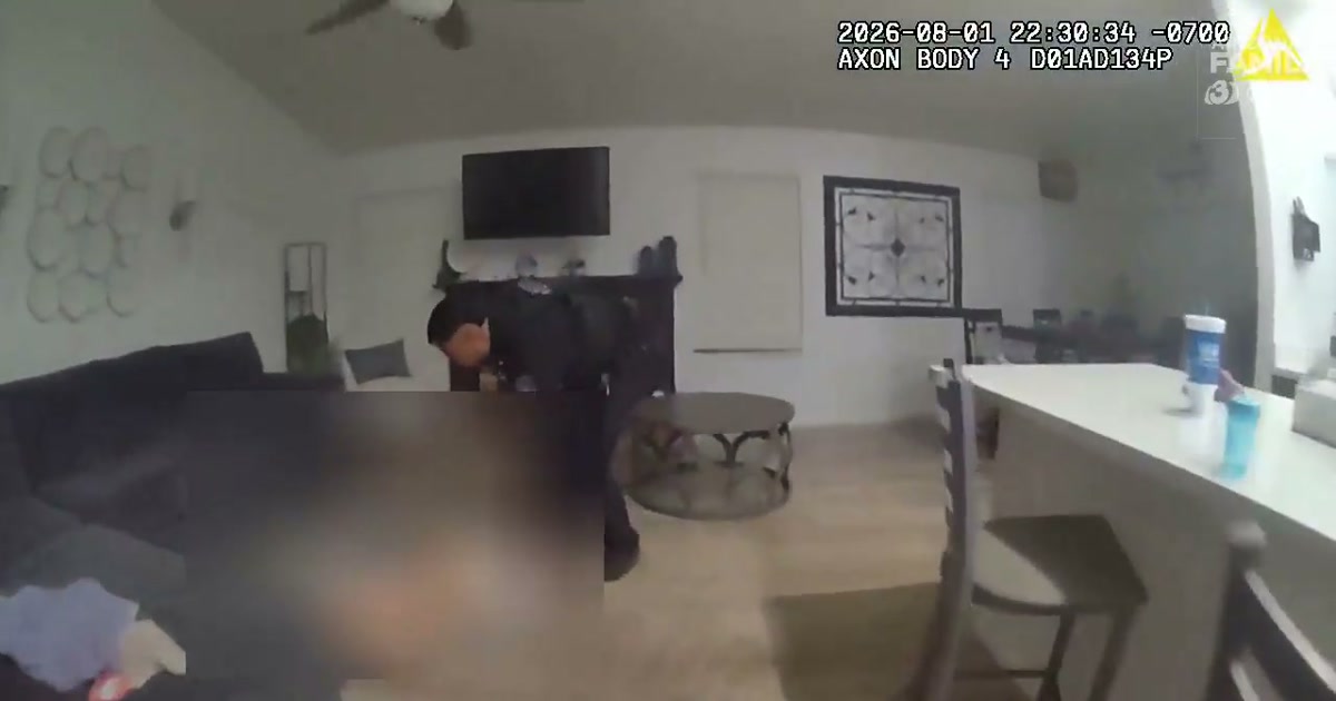 Genuine Glendale Police Department body-camera frame published by Arizona's Family showing an officer reaching a source-blurred 2-year-old in a car seat inside a smoke-filled home.