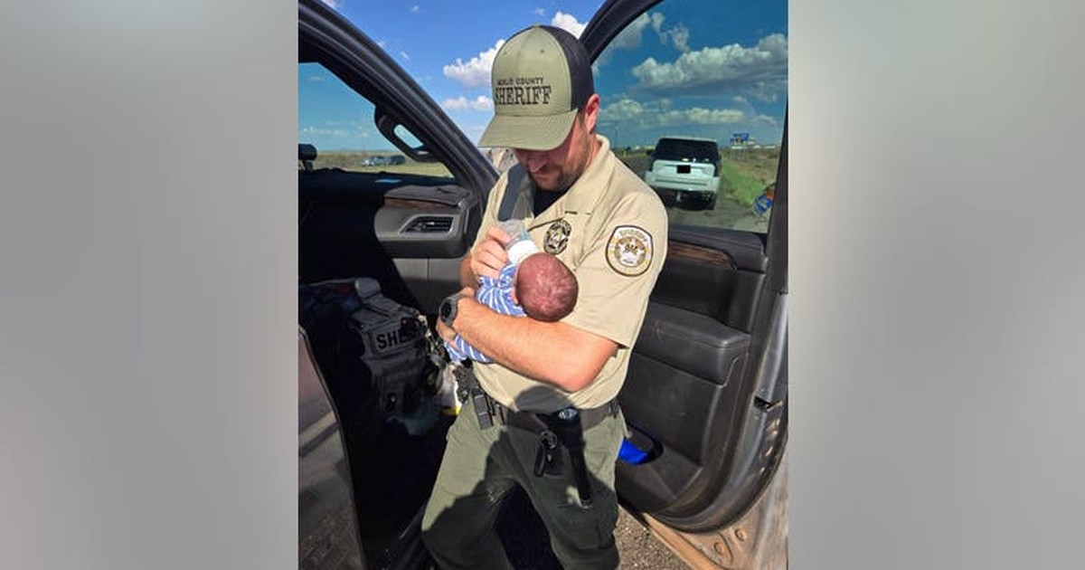 Navajo County Sheriff's deputy bottle-feeding the safely recovered newborn beside a patrol vehicle
