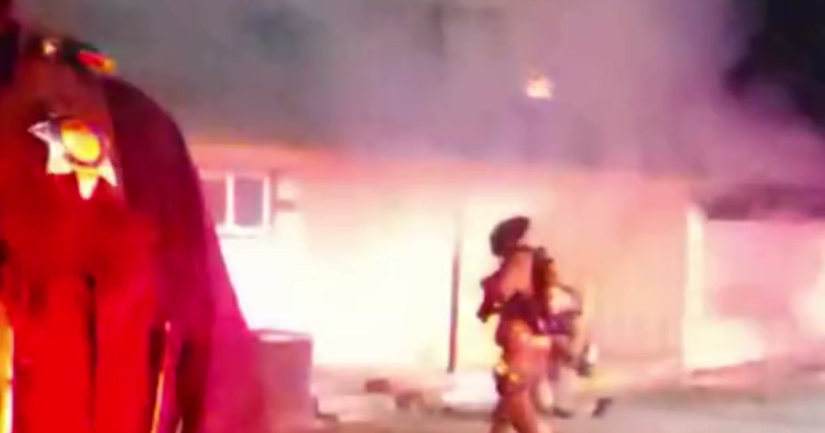 Fresno police and a firefighter outside a smoke-filled home during an early-morning attached-garage fire